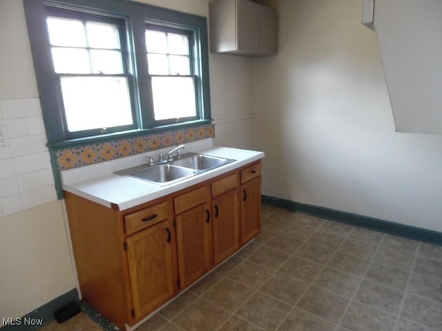 kitchen featuring brown cabinetry, light countertops, baseboards, and a sink