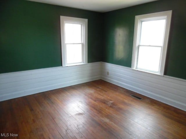 empty room with a wealth of natural light, visible vents, wainscoting, and hardwood / wood-style flooring