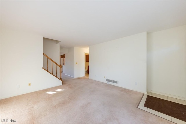 empty room featuring visible vents, light carpet, and stairway