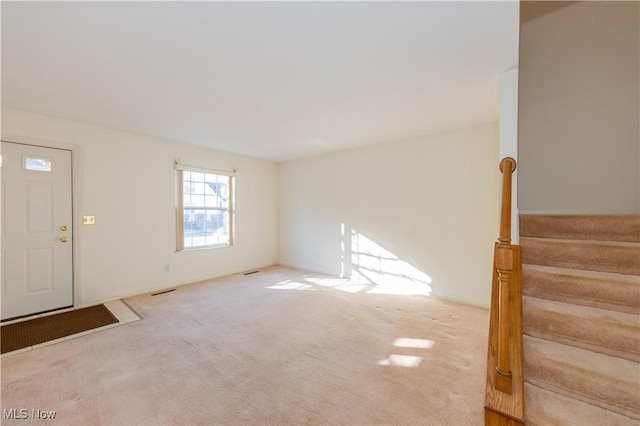 foyer entrance featuring stairway, visible vents, and carpet