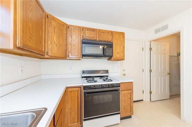 kitchen with visible vents, light countertops, white range oven, black microwave, and brown cabinets