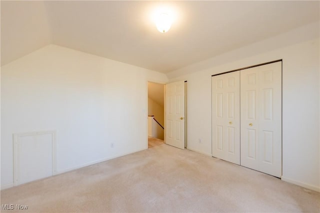 unfurnished bedroom featuring a closet, lofted ceiling, and light colored carpet