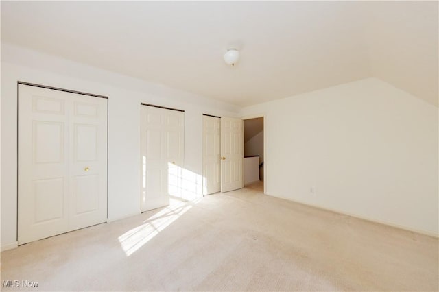 unfurnished bedroom with lofted ceiling, light colored carpet, and multiple closets