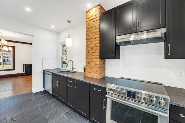 kitchen with a sink, under cabinet range hood, decorative backsplash, stainless steel appliances, and dark cabinets