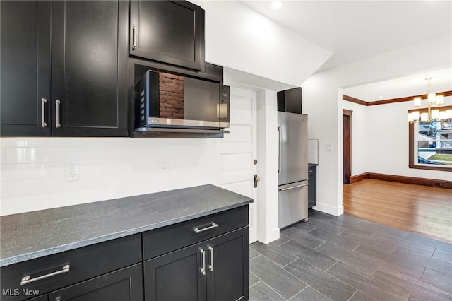 kitchen with baseboards, dark wood finished floors, dark cabinetry, a notable chandelier, and stainless steel appliances