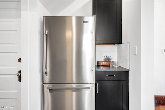 kitchen with decorative backsplash, dark countertops, dark cabinetry, and freestanding refrigerator