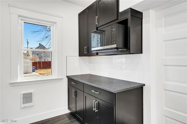 kitchen with baseboards, visible vents, black microwave, dark countertops, and tasteful backsplash