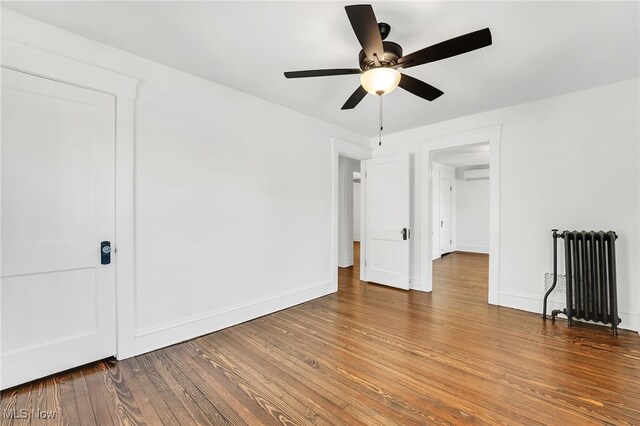 spare room featuring a wall mounted air conditioner, a ceiling fan, wood-type flooring, radiator, and baseboards