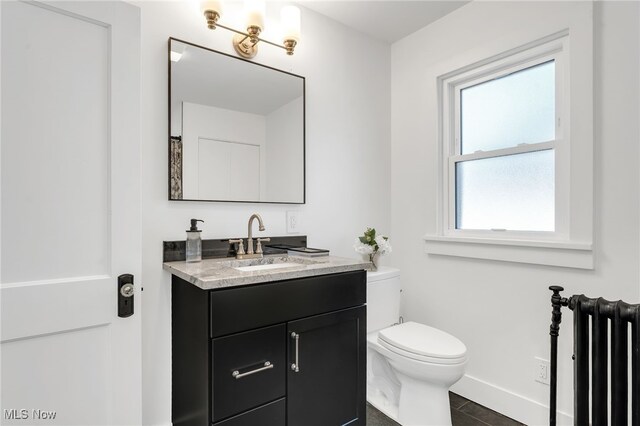 bathroom featuring vanity, toilet, radiator heating unit, and baseboards