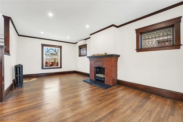 unfurnished living room featuring a brick fireplace, baseboards, ornamental molding, recessed lighting, and hardwood / wood-style flooring