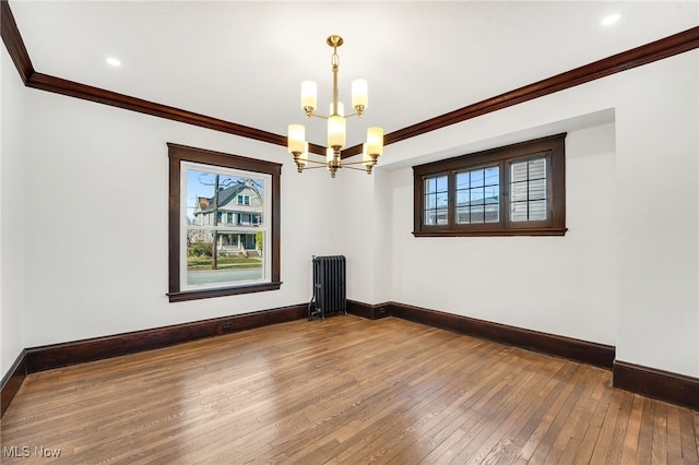 unfurnished room with ornamental molding, hardwood / wood-style floors, radiator heating unit, an inviting chandelier, and baseboards