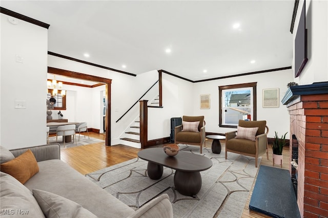 living area with ornamental molding, wood finished floors, an inviting chandelier, a fireplace, and stairs