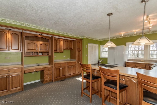 kitchen with brown cabinetry, a sink, a textured ceiling, decorative light fixtures, and dark carpet