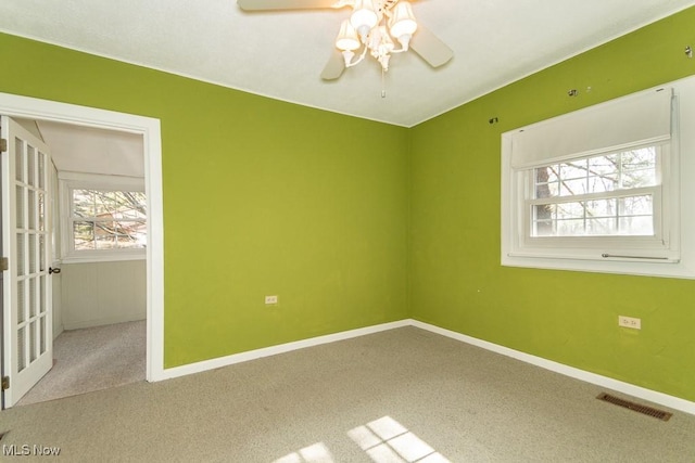 carpeted spare room with visible vents, baseboards, and ceiling fan