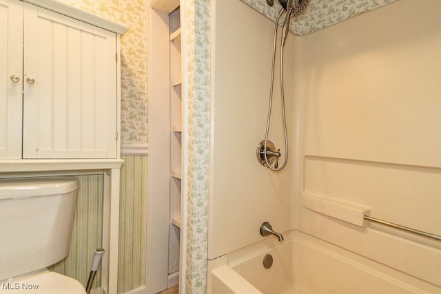 bathroom with wallpapered walls,  shower combination, toilet, and a wainscoted wall