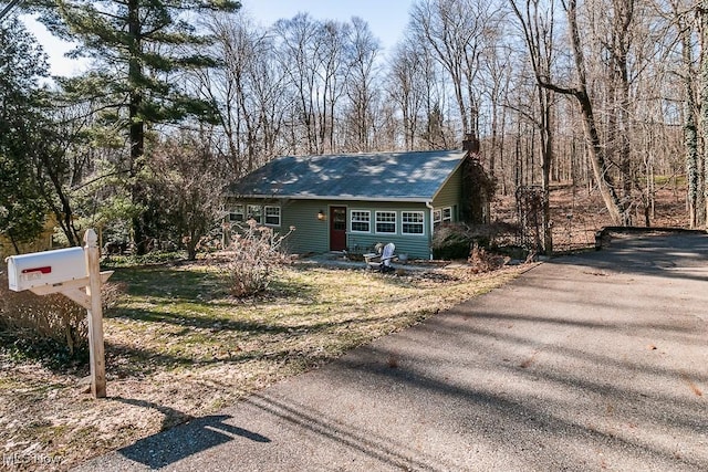 view of front facade featuring aphalt driveway, roof with shingles, and a chimney