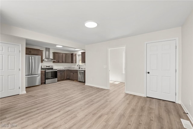 kitchen featuring a sink, light countertops, dark brown cabinetry, appliances with stainless steel finishes, and wall chimney range hood