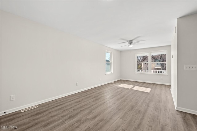 spare room with wood finished floors, a ceiling fan, visible vents, and baseboards