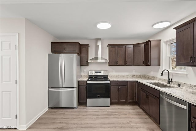 kitchen with dark brown cabinets, light wood-type flooring, appliances with stainless steel finishes, wall chimney exhaust hood, and a sink