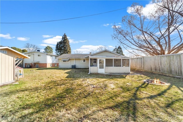 back of house featuring central AC unit, fence, a sunroom, a fire pit, and a lawn