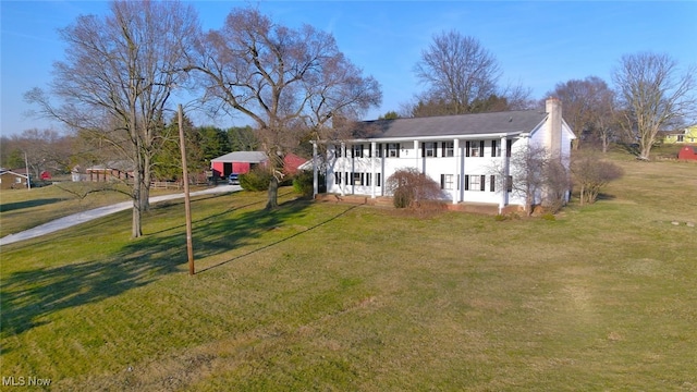 rear view of house featuring a lawn, driveway, and a chimney