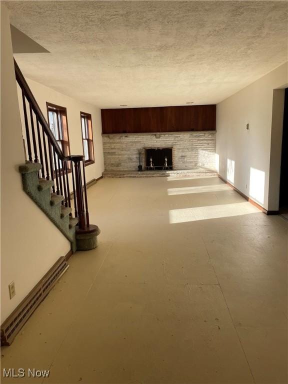 unfurnished living room with baseboards, a textured ceiling, concrete floors, and stairs