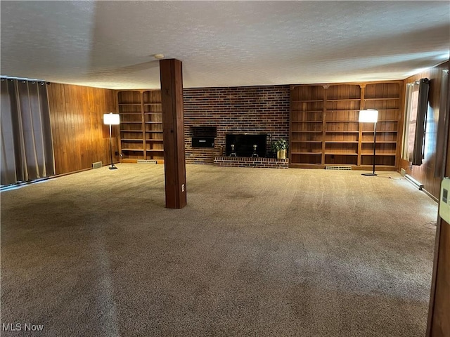 unfurnished living room featuring a textured ceiling, wooden walls, a fireplace, and carpet