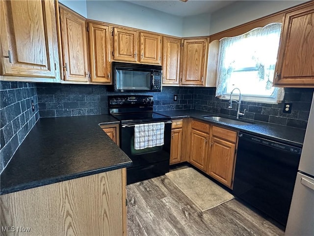 kitchen featuring black appliances, wood finished floors, dark countertops, and a sink