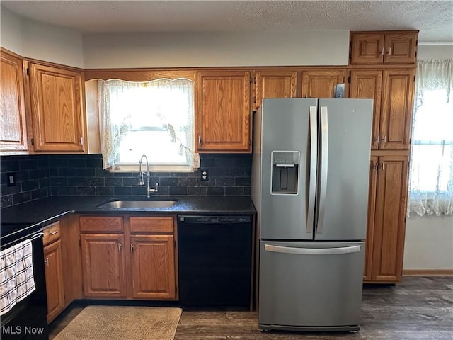 kitchen with brown cabinetry, dark wood finished floors, a sink, black appliances, and dark countertops