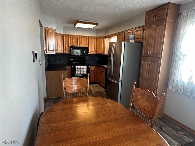 kitchen with black appliances, dark countertops, a textured ceiling, dark wood finished floors, and decorative backsplash