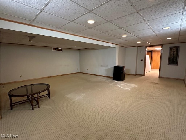 finished basement featuring visible vents, light colored carpet, baseboards, and a drop ceiling