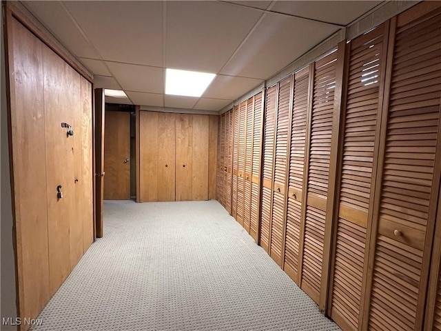 corridor with light carpet, wooden walls, and a paneled ceiling