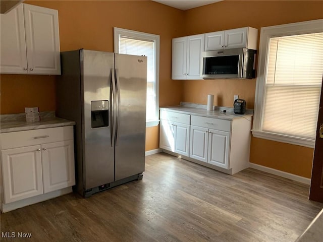 kitchen with white cabinetry, stainless steel appliances, light wood-type flooring, and baseboards