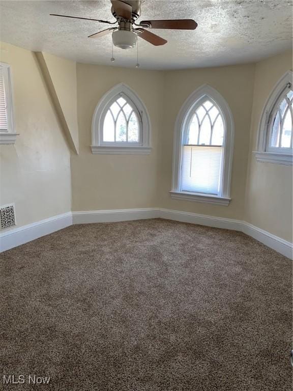 carpeted spare room with visible vents, a textured ceiling, baseboards, and a ceiling fan