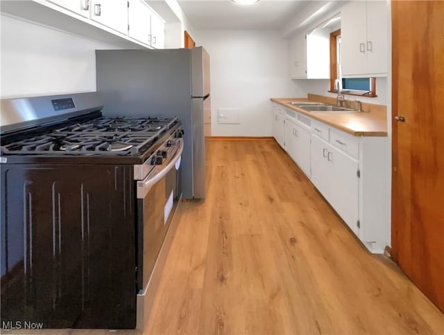 kitchen featuring light wood-type flooring, light countertops, stainless steel gas stove, white cabinetry, and a sink