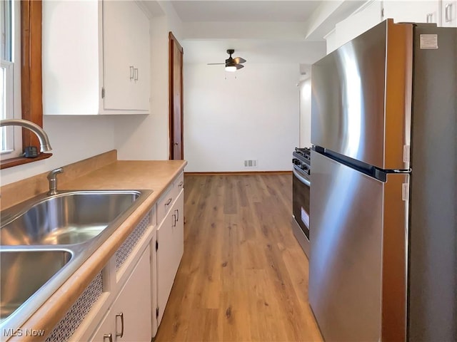 kitchen featuring a sink, stainless steel appliances, white cabinets, light wood finished floors, and ceiling fan