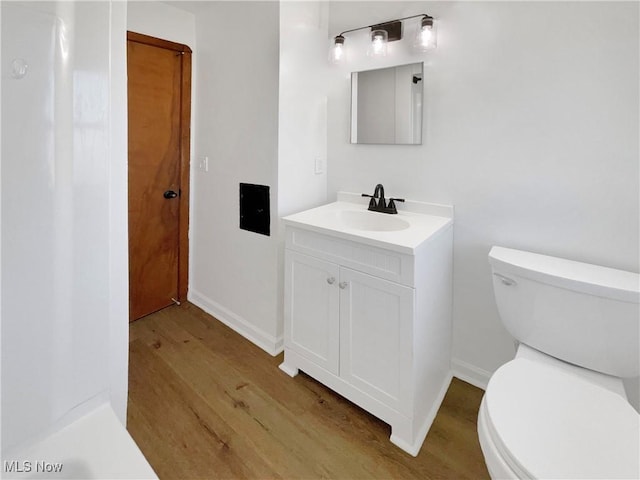 bathroom featuring baseboards, toilet, wood finished floors, and vanity