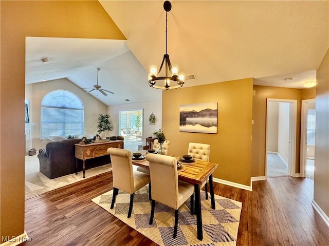 dining space with vaulted ceiling, ceiling fan with notable chandelier, baseboards, and wood finished floors