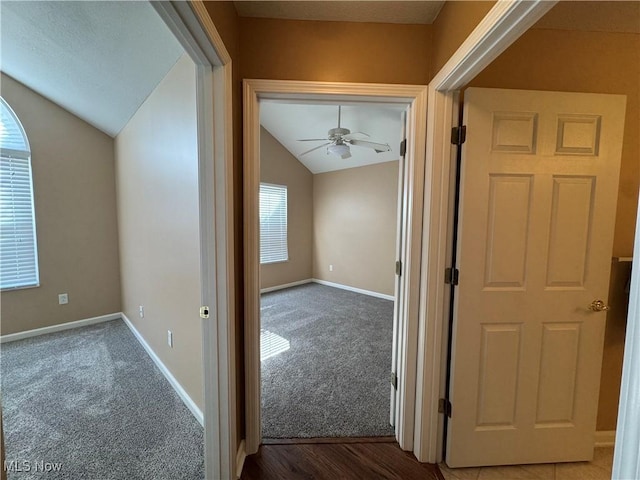 hallway with carpet flooring, baseboards, and vaulted ceiling