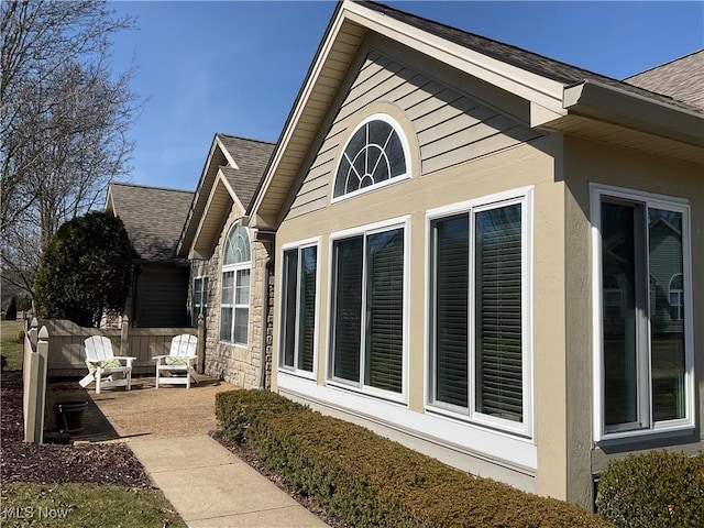 view of property exterior featuring a shingled roof, stone siding, and stucco siding