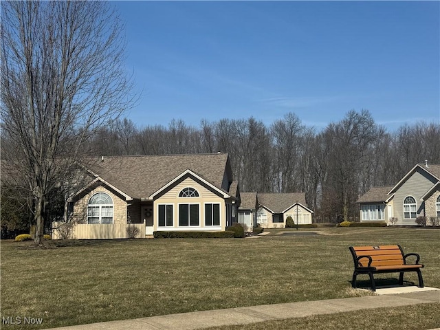 view of front of property featuring stone siding, a front yard, and roof with shingles