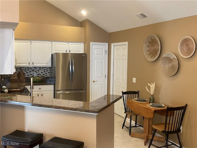 kitchen featuring backsplash, white cabinetry, freestanding refrigerator, a peninsula, and lofted ceiling