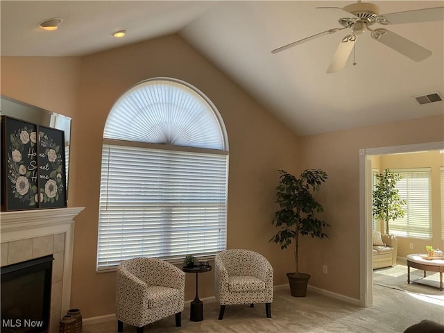 living area featuring visible vents, carpet flooring, ceiling fan, vaulted ceiling, and a tile fireplace