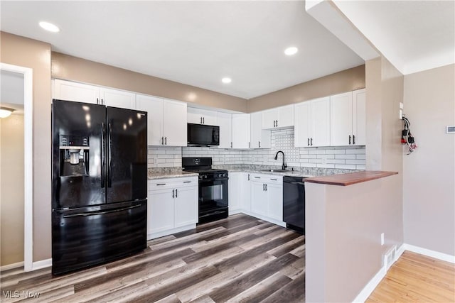 kitchen with wood finished floors, white cabinetry, black appliances, and a sink