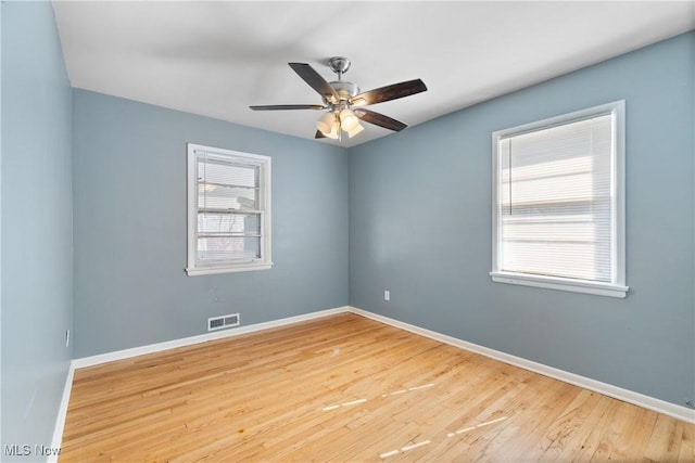 spare room with ceiling fan, visible vents, baseboards, and wood finished floors