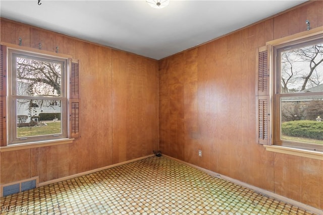 spare room with visible vents, plenty of natural light, wooden walls, and baseboards