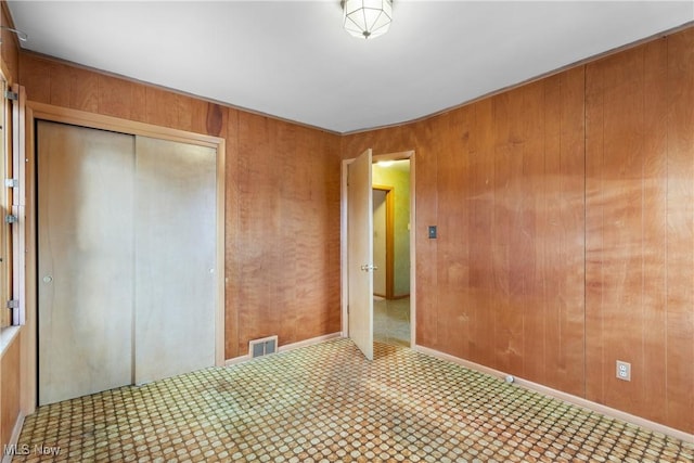 unfurnished bedroom with tile patterned floors, visible vents, a closet, wood walls, and baseboards