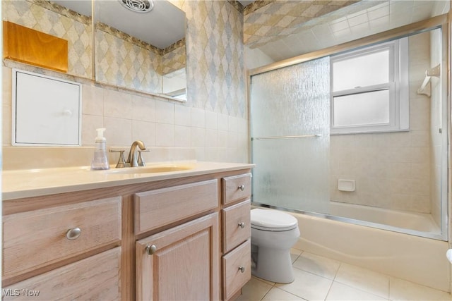 bathroom featuring tile patterned flooring, toilet, vanity, combined bath / shower with glass door, and tile walls