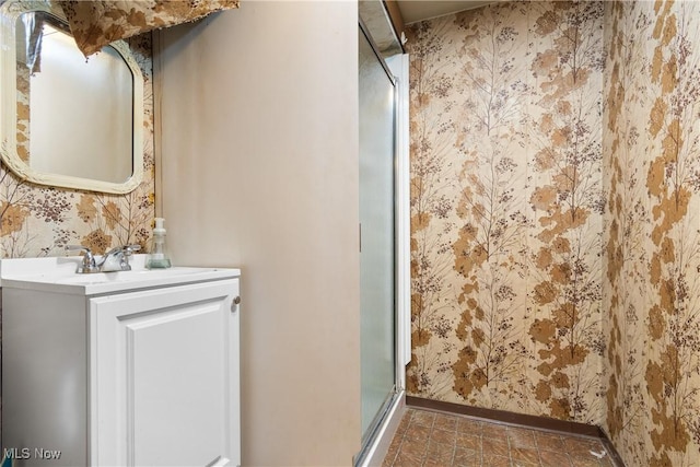 bathroom featuring baseboards, vanity, a shower stall, and wallpapered walls