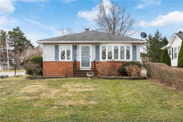 bungalow featuring brick siding, entry steps, a front yard, roof with shingles, and a chimney